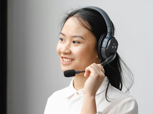 Smiling Asian woman with headset providing customer support in an office setting.